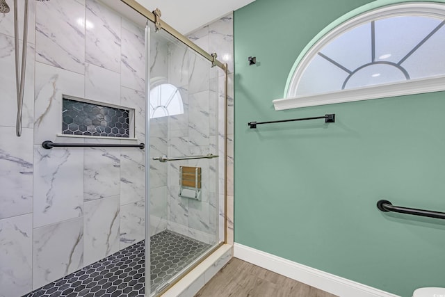 full bath featuring a marble finish shower, baseboards, and wood finished floors
