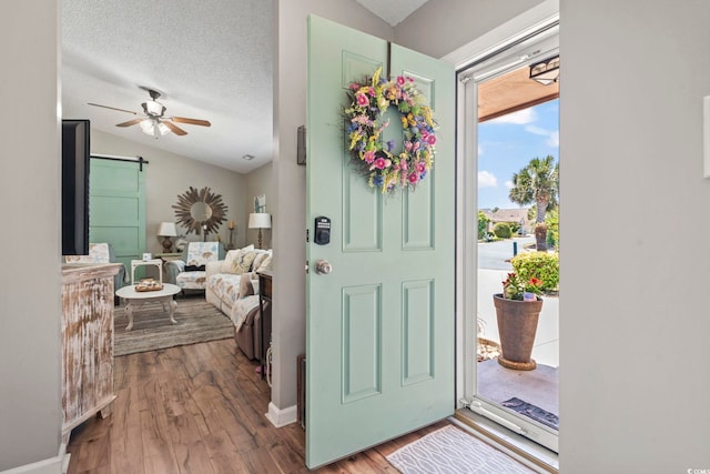 foyer entrance with wood finished floors, lofted ceiling, baseboards, a barn door, and a ceiling fan