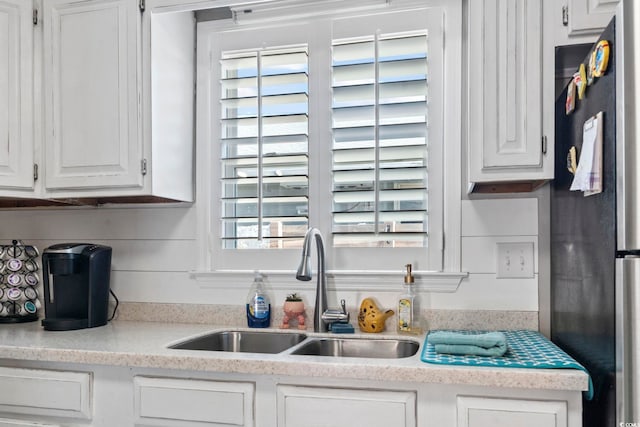 kitchen with a sink, light countertops, freestanding refrigerator, and white cabinetry