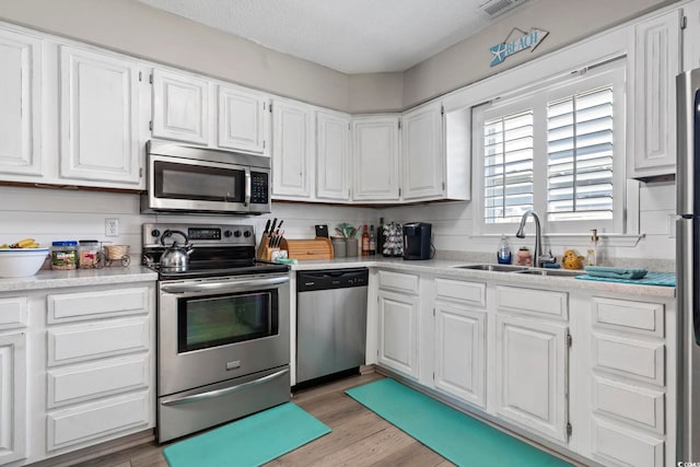 kitchen featuring white cabinets, a sink, light wood finished floors, light countertops, and stainless steel appliances