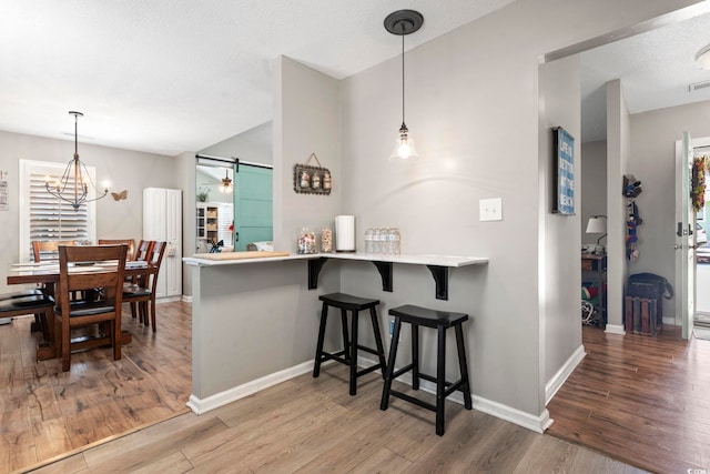 kitchen with a kitchen breakfast bar, baseboards, hanging light fixtures, and wood finished floors