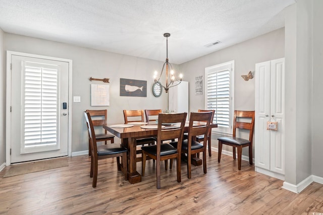 dining space with a textured ceiling, baseboards, an inviting chandelier, and light wood-style floors