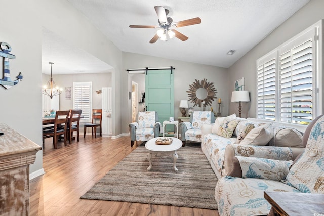 living room with visible vents, vaulted ceiling, a barn door, wood finished floors, and ceiling fan with notable chandelier