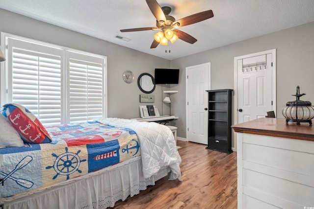bedroom with ceiling fan, visible vents, and wood finished floors