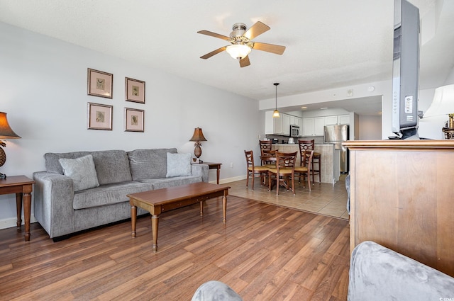 living room featuring light wood-type flooring, baseboards, and ceiling fan