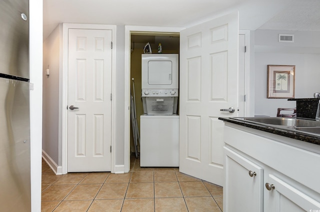 laundry room featuring laundry area, visible vents, baseboards, stacked washer / drying machine, and light tile patterned floors