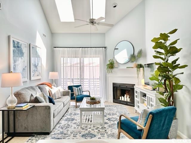 living room with high vaulted ceiling, a skylight, ceiling fan, and a fireplace
