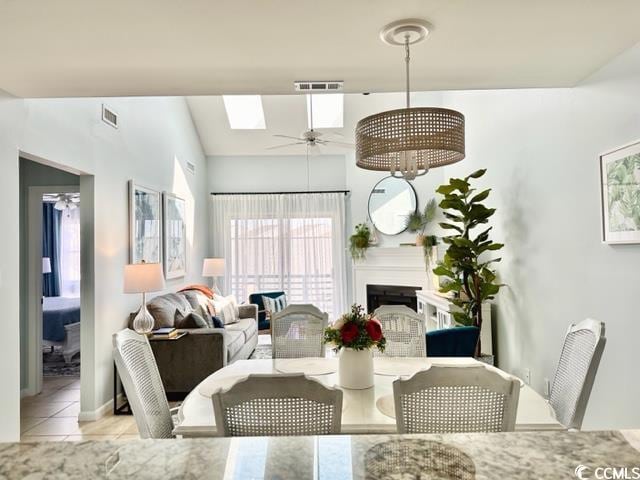 tiled dining area featuring ceiling fan, visible vents, a skylight, and a fireplace