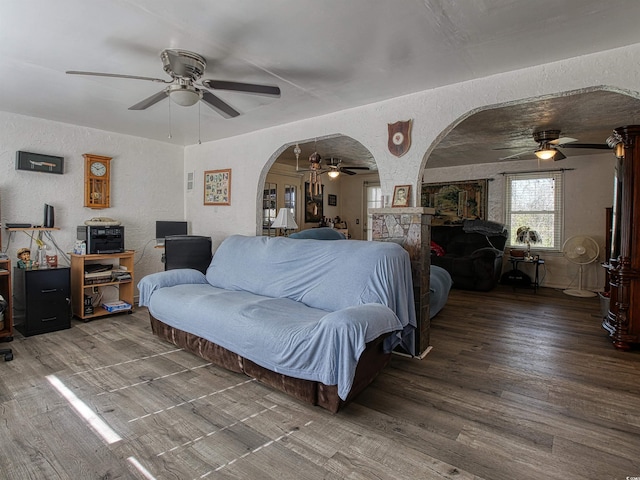 living room with arched walkways, ceiling fan, a textured wall, and wood finished floors
