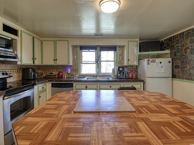 kitchen with range hood, a sink, backsplash, green cabinets, and stainless steel appliances