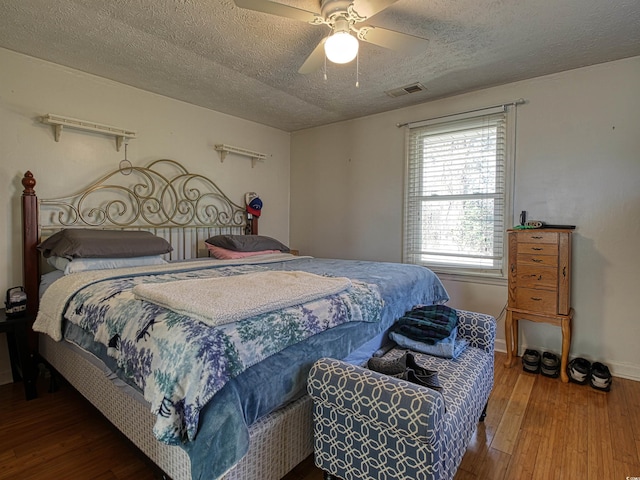 bedroom with visible vents, hardwood / wood-style floors, baseboards, a textured ceiling, and a ceiling fan