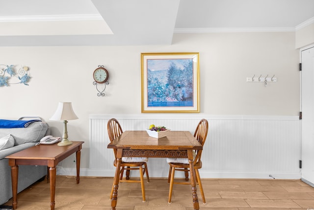 dining room featuring light wood-style floors, baseboards, crown molding, and a wainscoted wall