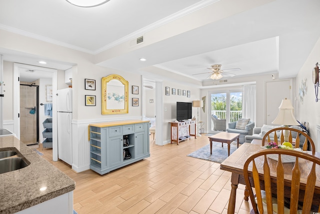 living area with crown molding, ceiling fan, a raised ceiling, light wood finished floors, and visible vents