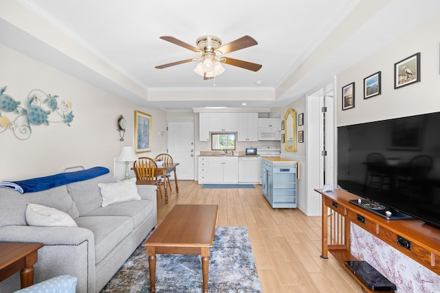 living room featuring crown molding, a raised ceiling, ceiling fan, and light wood-style flooring