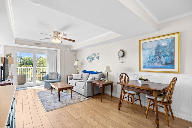 living room featuring light wood-type flooring, a ceiling fan, a tray ceiling, and ornamental molding