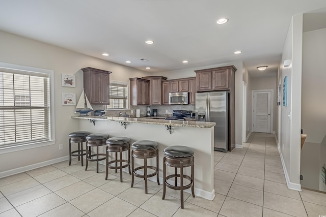kitchen featuring a peninsula, appliances with stainless steel finishes, light tile patterned floors, and a kitchen bar