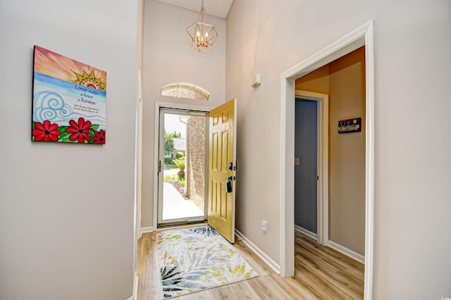 entrance foyer with baseboards, an inviting chandelier, a high ceiling, and light wood-type flooring