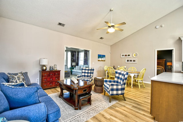 living area featuring high vaulted ceiling, ceiling fan, light wood-style flooring, and visible vents