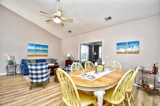 dining space with a ceiling fan, light wood finished floors, lofted ceiling, and visible vents
