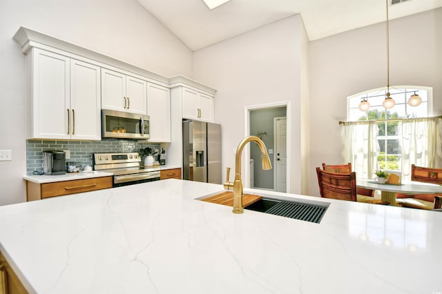 kitchen featuring high vaulted ceiling, tasteful backsplash, a sink, appliances with stainless steel finishes, and hanging light fixtures