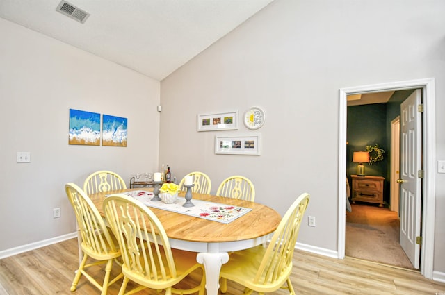 dining room with baseboards, visible vents, light wood finished floors, and high vaulted ceiling