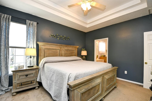 bedroom with light colored carpet, baseboards, ensuite bath, and a tray ceiling