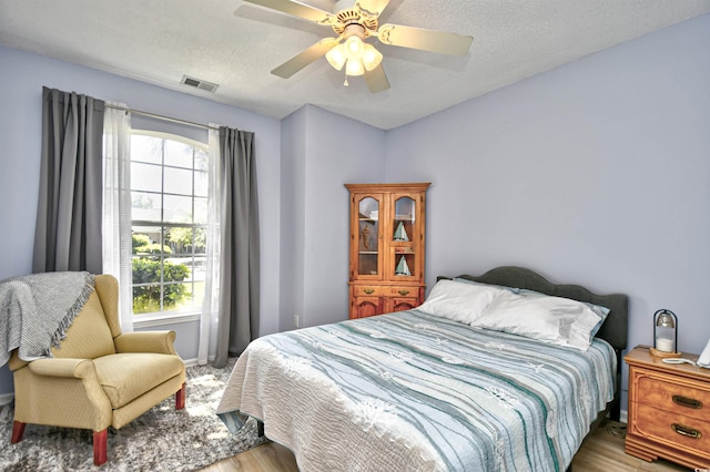 bedroom featuring a textured ceiling, ceiling fan, wood finished floors, and visible vents