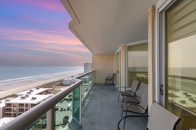 balcony at dusk featuring a water view and a view of the beach