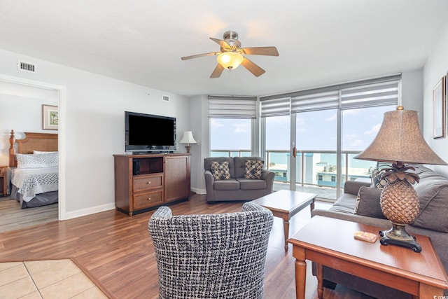 living area featuring visible vents, wood finished floors, a wall of windows, baseboards, and a ceiling fan