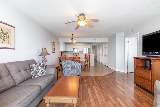 living area featuring baseboards, ceiling fan with notable chandelier, and wood finished floors