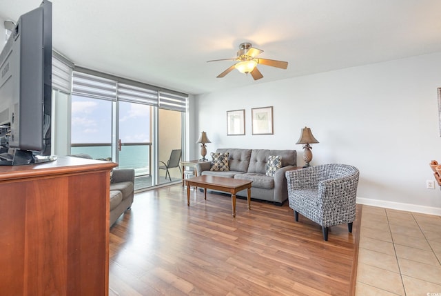 living room featuring baseboards, a ceiling fan, light wood finished floors, and floor to ceiling windows