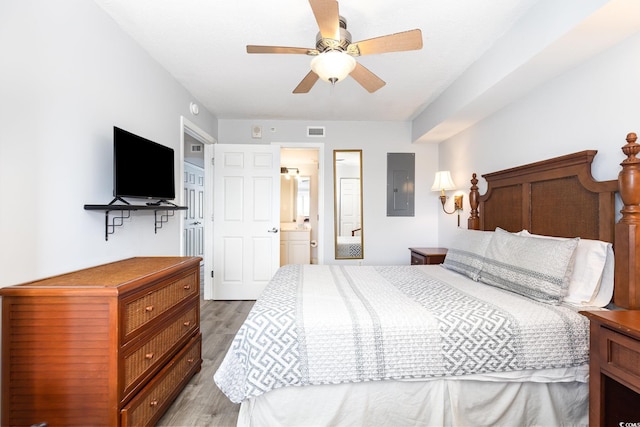 bedroom featuring visible vents, ensuite bathroom, light wood-type flooring, electric panel, and a ceiling fan