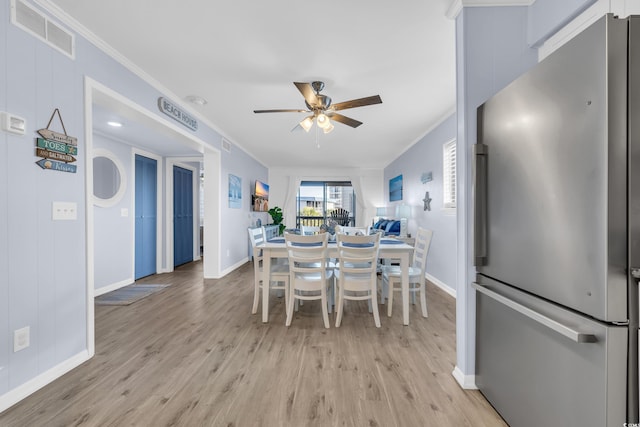 dining space featuring visible vents, ornamental molding, baseboards, ceiling fan, and light wood-style flooring