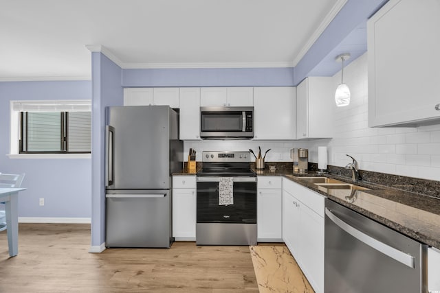 kitchen featuring a sink, dark stone counters, stainless steel appliances, decorative backsplash, and ornamental molding
