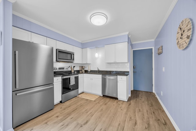 kitchen featuring dark countertops, a sink, light wood finished floors, ornamental molding, and stainless steel appliances