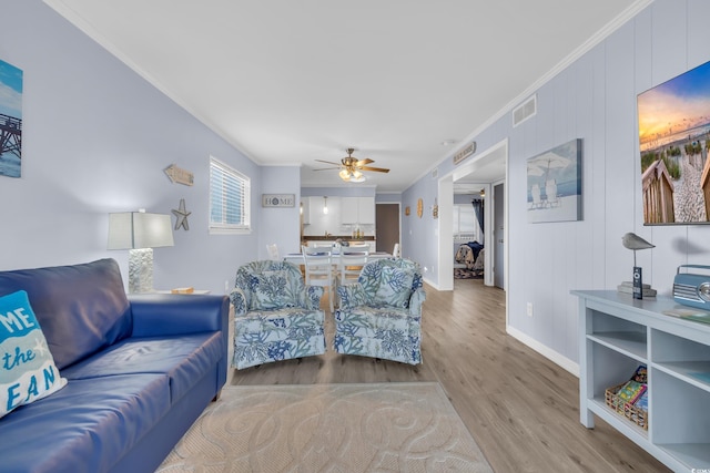 living room with crown molding, visible vents, wood finished floors, baseboards, and ceiling fan