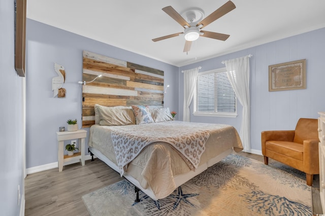 bedroom featuring a ceiling fan, wood finished floors, baseboards, wooden walls, and ornamental molding