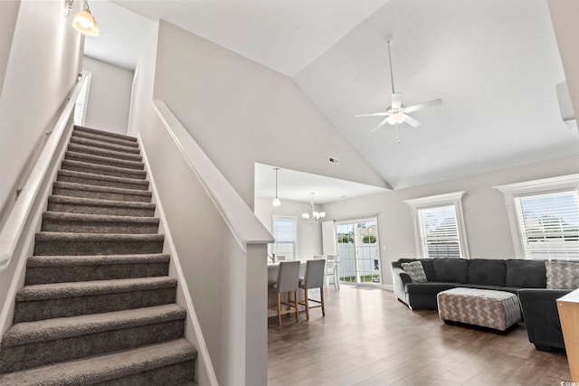 living area with stairway, high vaulted ceiling, ceiling fan with notable chandelier, and wood finished floors