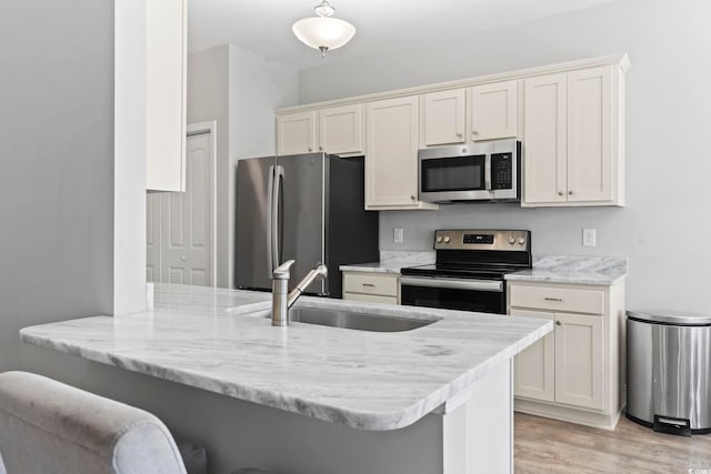 kitchen with appliances with stainless steel finishes, light stone countertops, light wood-type flooring, a sink, and a peninsula