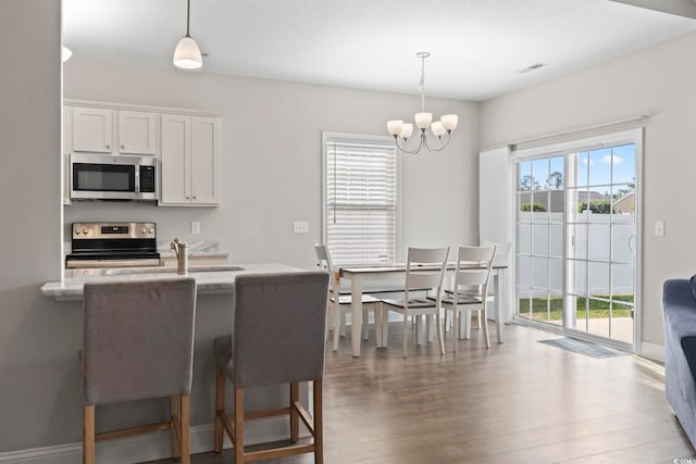 kitchen with hanging light fixtures, an inviting chandelier, stainless steel appliances, white cabinetry, and wood finished floors