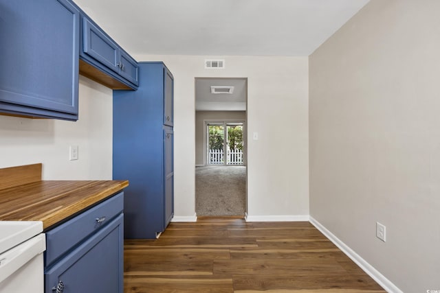 kitchen featuring dark wood-type flooring, wooden counters, blue cabinetry, and visible vents