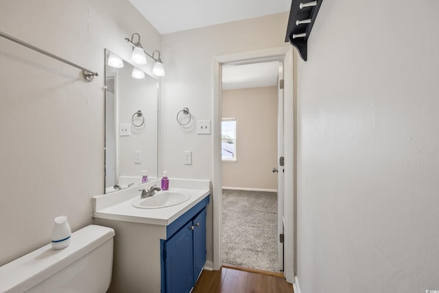 half bathroom with vanity, baseboards, toilet, and wood finished floors