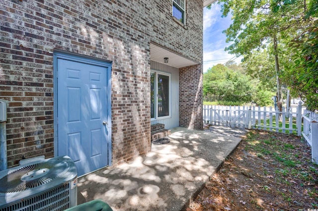 doorway to property with brick siding, central AC, and fence
