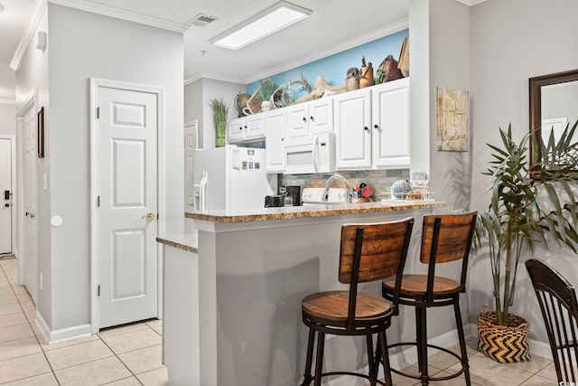 kitchen featuring light tile patterned floors, decorative backsplash, a kitchen breakfast bar, and white appliances