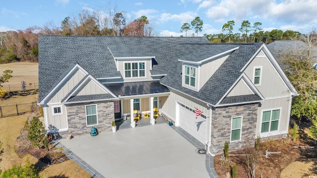 craftsman inspired home featuring a shingled roof, board and batten siding, fence, and stone siding
