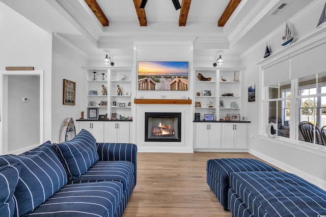 living room with visible vents, crown molding, beam ceiling, a large fireplace, and light wood-style flooring