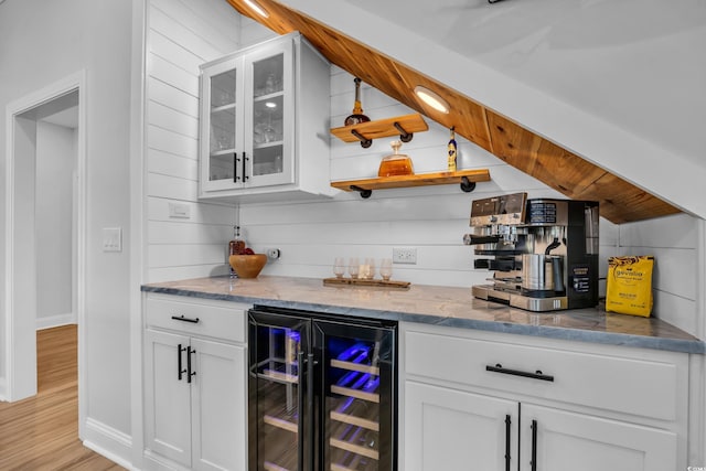 bar with a dry bar, vaulted ceiling, baseboards, beverage cooler, and light wood-style flooring