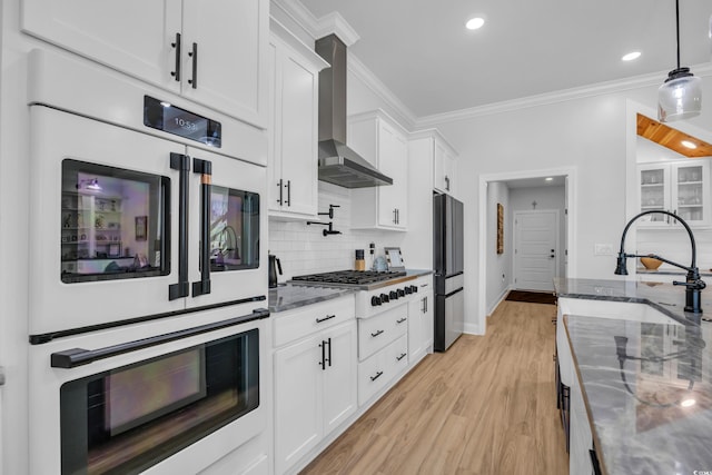 kitchen with freestanding refrigerator, double oven, wall chimney exhaust hood, a sink, and stainless steel gas stovetop