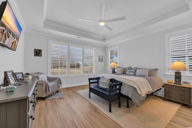 bedroom featuring baseboards, ornamental molding, a tray ceiling, and light wood-style flooring