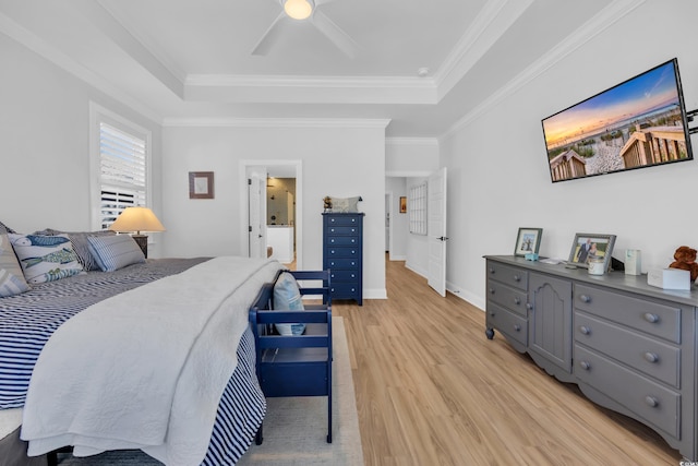bedroom featuring a ceiling fan, a tray ceiling, ornamental molding, and light wood-style flooring